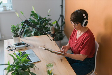 Portrait of mature woman wearing headphones and talking at online radio station - podcast and...