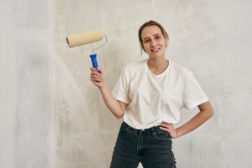 pretty young woman holding a paint roller in her hands. house renovation, wall painting
