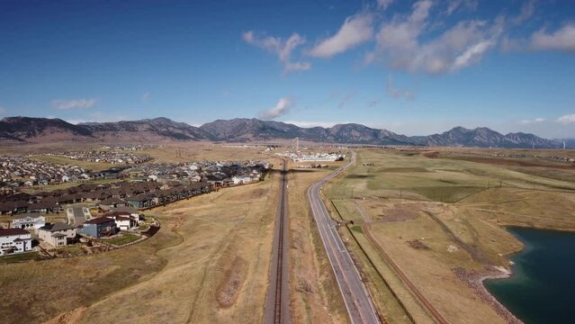 Following the train tracks and road in the Rocky Flats towards the Rocky Mountains, aerial