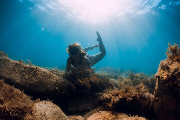 Young woman explore bottom with seaweed. Free diver girl with mask and sun light in blue ocean