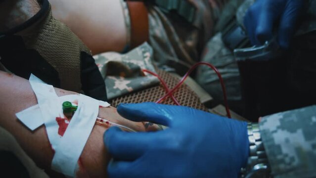 Military medic glue the patch during receiving blood transfusion. Provides first aid to a soldier who inserts a needle into a vein