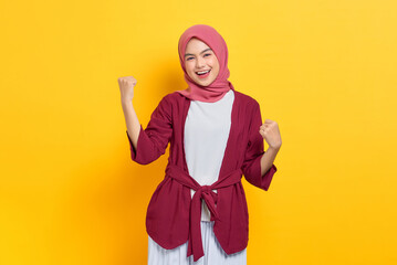 Fototapeta na wymiar Excited beautiful Asian woman in casual shirt celebrating big luck and success with raised fists isolated over yellow background