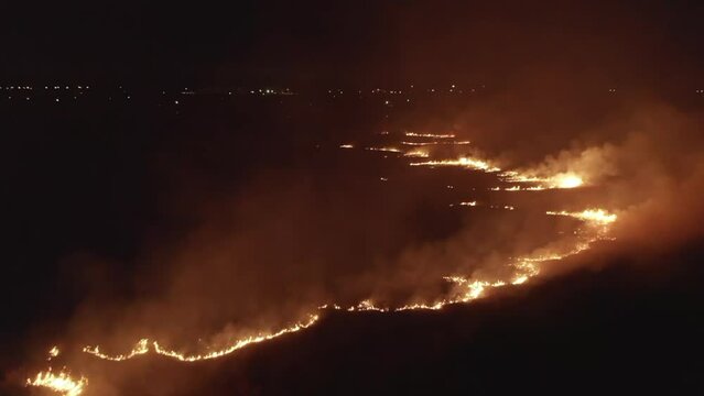 forest fire at night, aerial drone view, lights of city on background