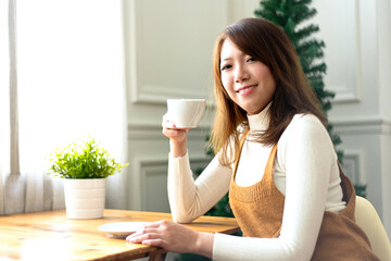 Young and pretty Asian girl with cup of coffee laughing in cafe