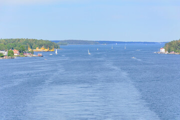 Obraz premium view of the Stockholm fiord from a ferry deck. Blue sea water, green forest on the shores, many small sailboats