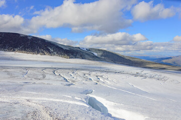 Norwegian landscape with snow covered mountain glacier and clouds. Dangerous crack in the ice