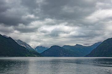 Obraz premium View of Geirangerfjord in Norway. Grey sea water, cloudy sky, dark green and blue mounain slopes