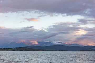 Evening landscape in Norway. Grey water of the fjord
Light blue sky with grey, pink and lilac clouds, misty mountains on the horizon