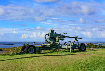 Fototapeta na wymiar Cannon at Ergan fortress world war II open air museum in Bud, Romsdal, Norway. Blue sky with clouds blue Atlantic Ocean water and green grass on the background