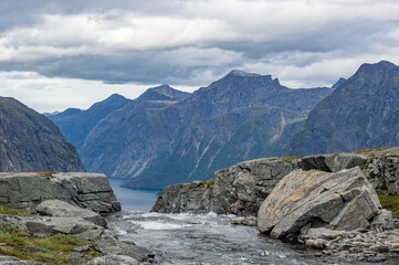 The source of Mardalsfossen waterfall in Norway. Dramatic cloudy sky, blue and grey mountains, white water of the mountain stream, mossy rocks around