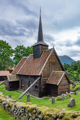Fototapeta na wymiar Rødven Stave Church. Medieval wooden viking era church in Norway. Dramatic cloudy sky, green grass and trees, ancient wooden walls, mossy cobblestone fence