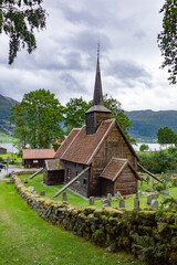 Fototapeta na wymiar Rødven Stave Church. Medieval wooden viking era church in Norway. Dramatic cloudy sky, green grass and trees, ancient wooden walls, mossy cobblestone fence