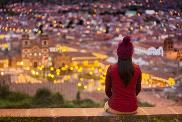 Turista sentada en el mirador mirando la plaza iluminada de Cuzco