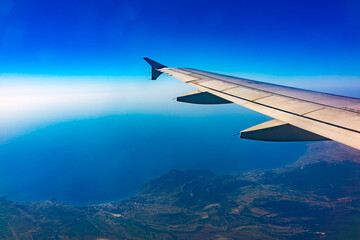View from the airplane window at a beautiful blue clear sky, earth, sea and the airplane wing