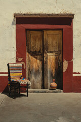 old wooden chair and door, clay jug and  traditional 
blanket  in old colonial mexican home