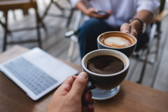 Closeup image of two businessman clinking coffee cups together while working and meeting with laptop computer on the table