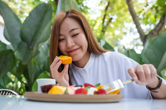 Portrait image  of a young woman holding a piece of an orange while eating mixed fruits french toast brunch in restaurant