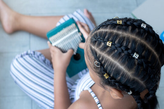 African Girl With Braided Hair   Playing Wooden Kalimba Instrument On Floor, Kalimba Or Thumb Piano Acoustic Music Instrument From Africa, View From Above