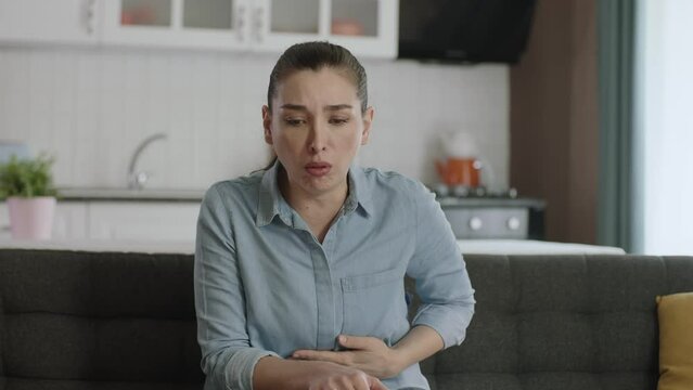 Sick young woman with stomachache, coughing.A young woman in her 30s having trouble breathing in the living room of her home. Shortness of breath, asthma, difficulty breathing. Coronavirus symptoms.