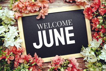 Welcome June typography text written on wooden blackboard with flower bouquet decorate on wooden...
