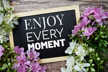 Enjoy Every Moment typography text written on wooden blackboard with flower bouquet decorate on wooden background