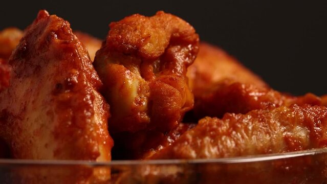 Cooked spicy buffalo wings smothered in hot sauce turning on table, close up shit