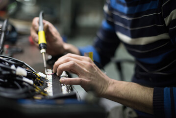 Industrial worker man soldering cables of manufacturing equipment in a factory. Selective focus