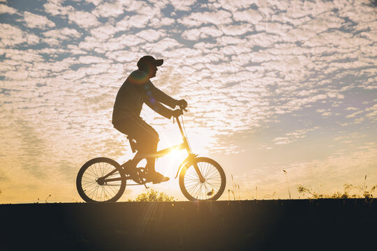 Silhouette of man relaxing, ride a bicycle along the bike lane in the park at the sunset.	