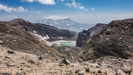 Turquoise acid lake on top of an active volcano. The layered structure of the steep slopes of the crater, melted snow is visible. Rocky ground in the foreground. Kamchatka. Gorely Volcano