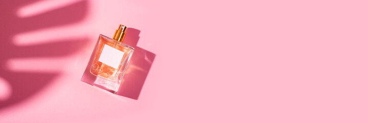 Transparent bottle of perfume with label on a pink background. Fragrance presentation with...
