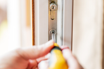 woman adjusting white pvc plastic balcony window door indoors. female using screwdriver to repair upvc window lock. house doors and windows maintenance concept. draft fixing conceptual