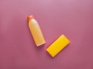 Top view of empty orange plastic containers. One for shampoo or lotion, the other for deodorant. Beauty concept for body and hair. Dark pink background. Copy space. Horizontal