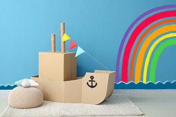 Toy cardboard ship in children's room near blue wall with painted rainbow