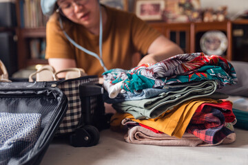 A woman folds clothes from a pile of selected belongings and puts them in luggage on the bed. Packing to go on a getaway vacation. Focus on clothes.