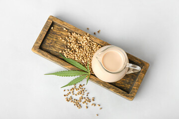 Wooden board with pitcher of hemp milk and seeds on white background