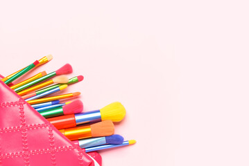Naklejka premium Cosmetic bag with set of colorful makeup brushes on pink background