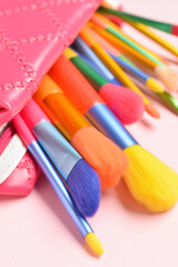 Cosmetic bag with set of colorful makeup brushes on pink background, closeup