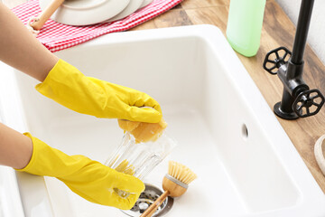 Woman in rubber gloves washing glass in sink, closeup