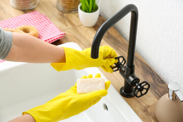Woman in rubber gloves wetting soap in sink, closeup