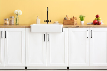 Counter with kitchen utensils and modern sink near color wall