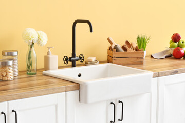 Fototapeta na wymiar Counter with modern sink, different kitchen utensils and chrysanthemum flowers near color wall