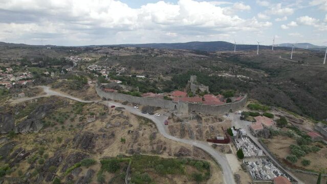 Aerial descending wide panoramic view of Sortelha village and wind turbines for eolic energy production in background. Portugal