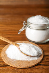 Pile of baking soda and spoon on wooden background