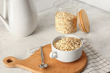 Wooden board with bowl of raw oatmeal on light background