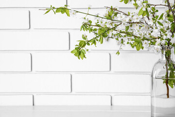 Vase with blooming tree branches on table near white brick wall