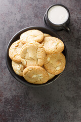 Fresh made Macadamia Cookies with white chocolate closeup in the black bowl and cup of milk on the table close-up. Vertical top view from above