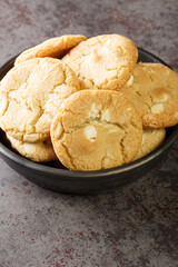 Fresh made Macadamia Cookies with white chocolate closeup in the black bowl on the table close-up. Vertical