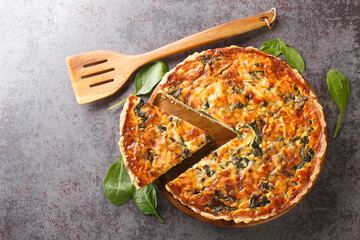 Savory tart of rich egg custard, spinach and cheese with cut out a slice on the plate on the gray table close-up. Hotizontal top view from above