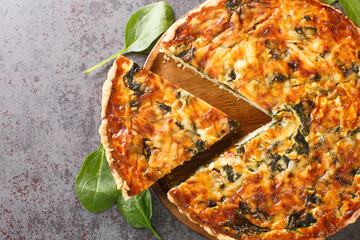 Quiche Florentine with spinach, cheese, eggs and spices on gray table with spatula, close-up....