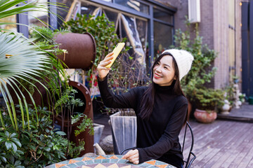 Stylish Young Asian beautiful woman using smart phone for in outdoor cafe at spring or autumn season. Blogger streaming broadcast for social media and communicating with followers